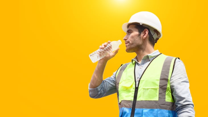 The construction worker drinks water to quench his thirst against a blank yellow background, he is wearing a safety vest and headgear