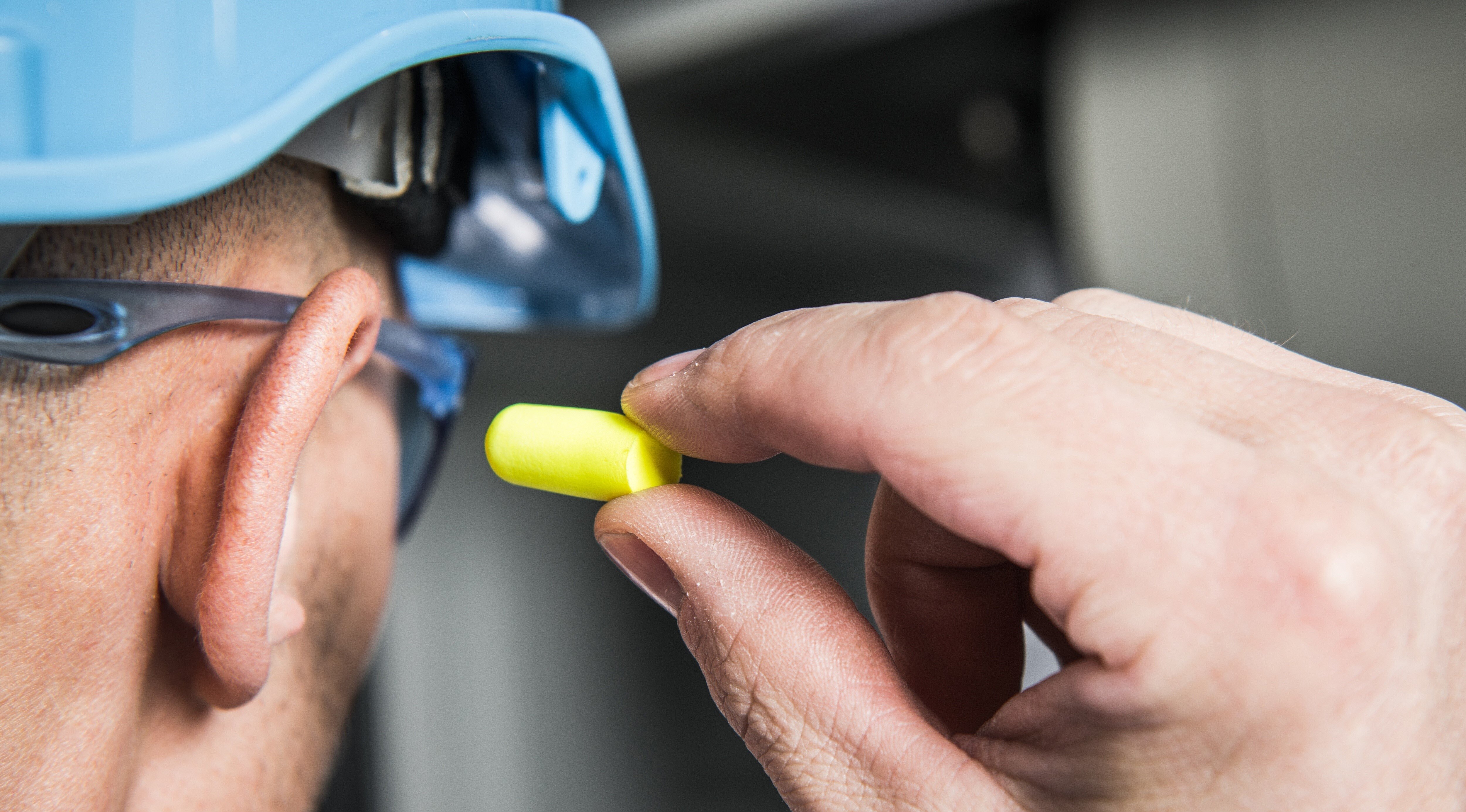 Man inserting Yellow Ear Plug for hearing protection